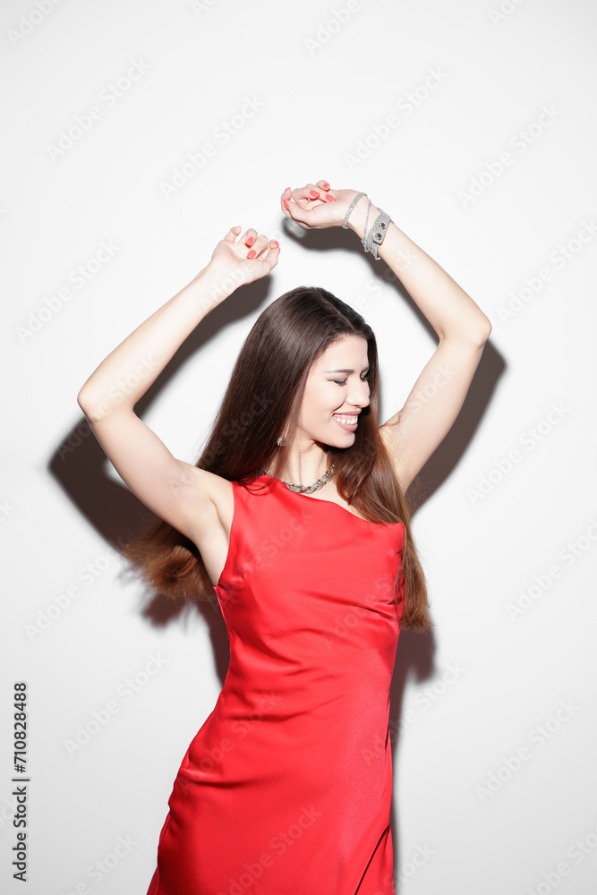 A joyful woman with long hair is captured mid-dance, wearing a bright red sleeveless dress against a stark white backdrop, expressing freedom and happiness. A joyful woman with long hair is captured mid-dance, wearing a bright red sleeveless dress against a stark white backdrop, expressing freedom and happiness.