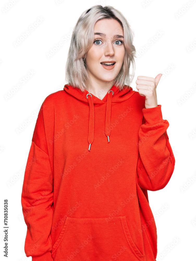 Young blonde girl wearing casual clothes smiling with happy face looking and pointing to the side with thumb up. Young blonde girl wearing casual clothes smiling with happy face looking and pointing to the side with thumb up.