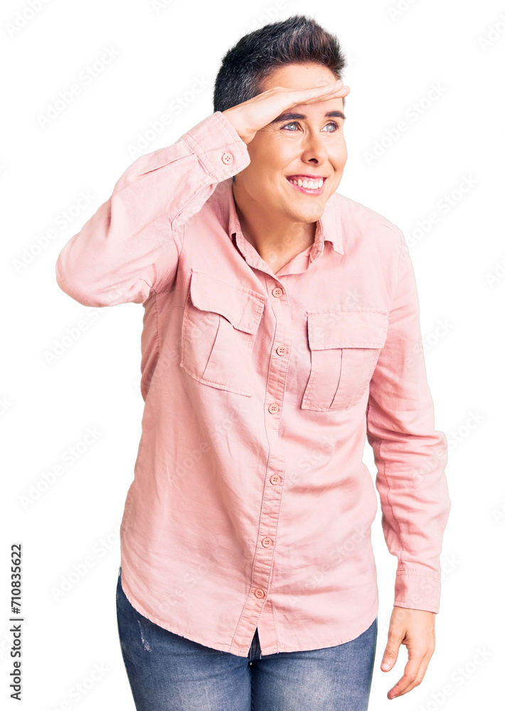 Young woman with short hair wearing casual clothes very happy and smiling looking far away with hand over head. searching concept. Young woman with short hair wearing casual clothes very happy and smiling looking far away with hand over head. searching concept.