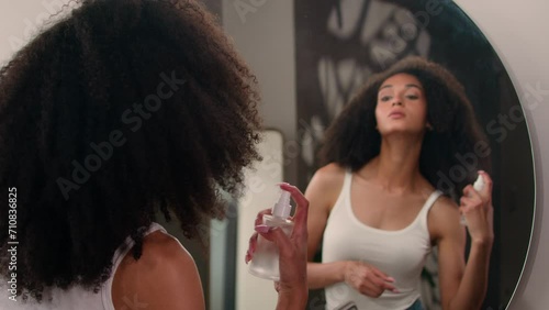 Mirror reflection in bathroom African American woman beautiful girl with gorgeous curly hair curls spraying thermal water on hairdo beauty routine apply spray for moisture anti-static product cosmetic photo