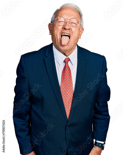 Senior man with grey hair wearing business suit and glasses sticking tongue out happy with funny expression. emotion concept.