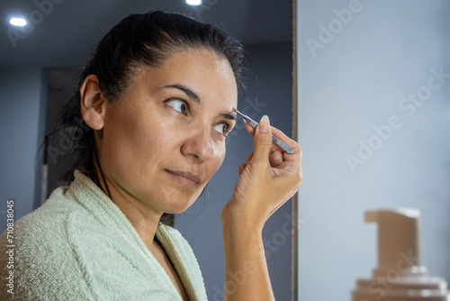 Latin woman using an eyebrow tweezer