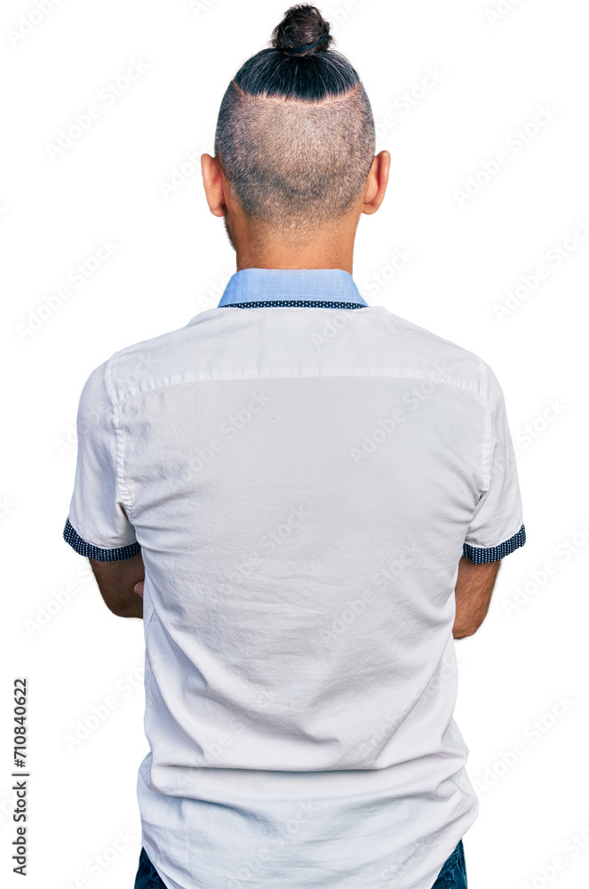 Hispanic man with ponytail wearing casual white shirt standing backwards looking away with crossed arms Hispanic man with ponytail wearing casual white shirt standing backwards looking away with crossed arms
