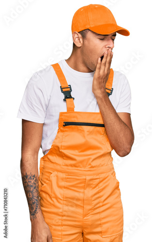 Young handsome african american man wearing handyman uniform bored yawning tired covering mouth with hand. restless and sleepiness.
