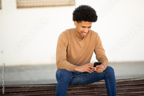 Happy man sitting outdoors on bench, holding phone
