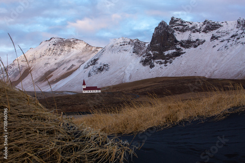 Picturesque, red-roofed church against snow-covered mountains with black sand beach in the foreground in Vik, Iceland 