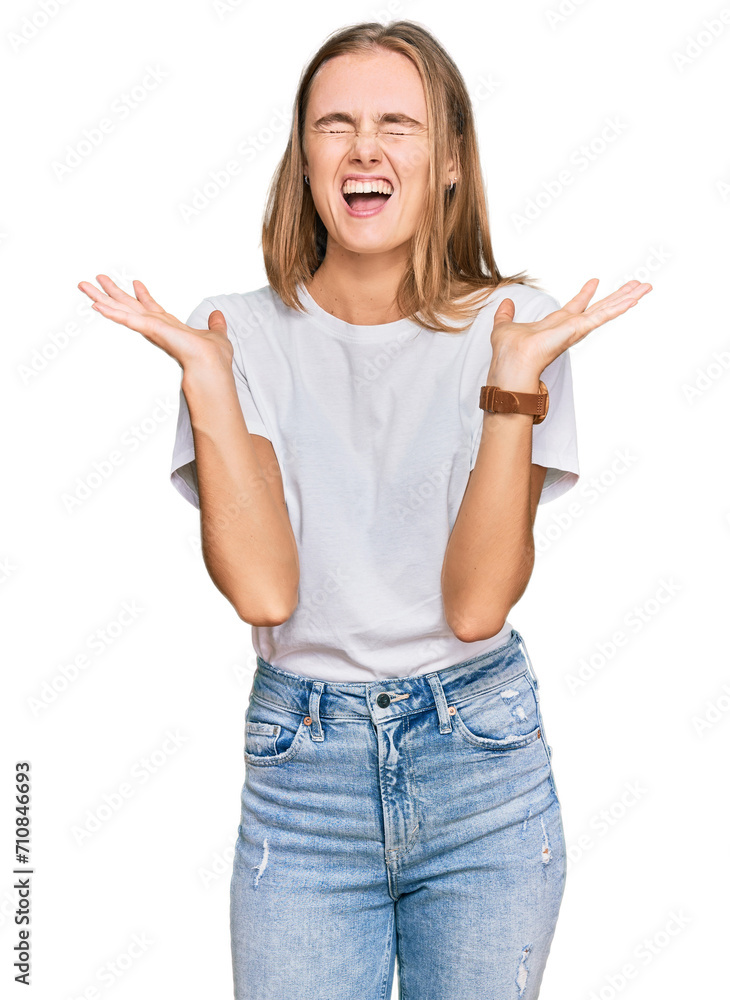 Beautiful young blonde woman wearing casual white t shirt celebrating mad and crazy for success with arms raised and closed eyes screaming excited. winner concept Beautiful young blonde woman wearing casual white t shirt celebrating mad and crazy for success with arms raised and closed eyes screaming excited. winner concept