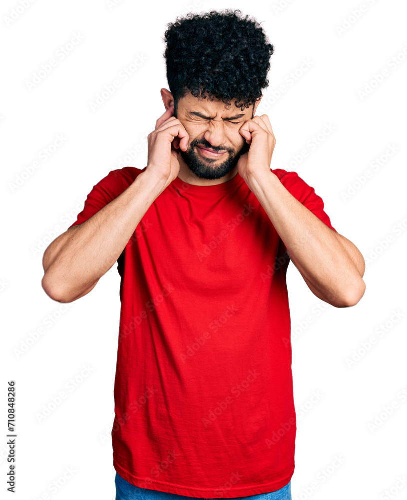Young arab man with beard wearing casual red t shirt covering ears with fingers with annoyed expression for the noise of loud music. deaf concept. Young arab man with beard wearing casual red t shirt covering ears with fingers with annoyed expression for the noise of loud music. deaf concept.