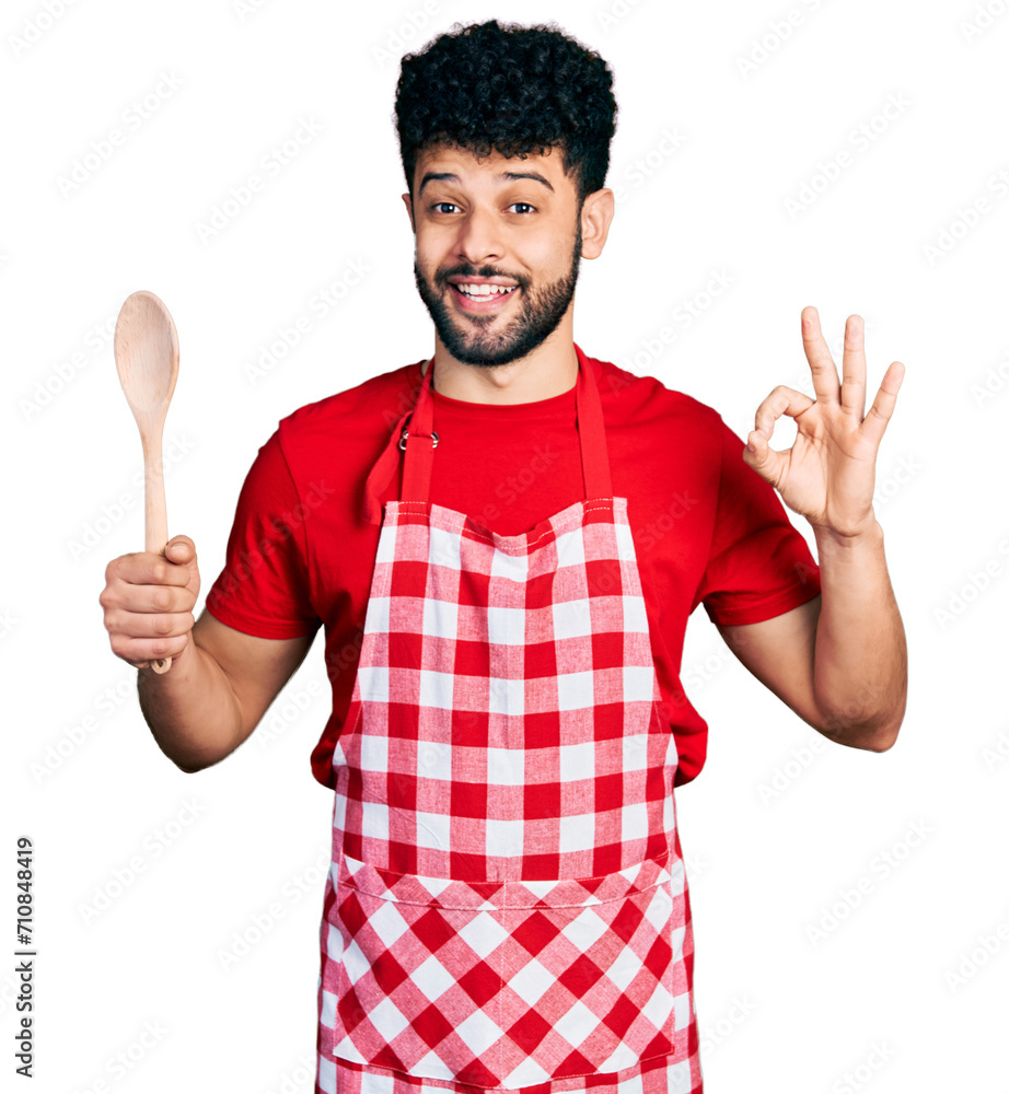Young arab man with beard wearing baker uniform holding wooden spoon celebrating crazy and amazed for success with open eyes screaming excited. Young arab man with beard wearing baker uniform holding wooden spoon celebrating crazy and amazed for success with open eyes screaming excited.