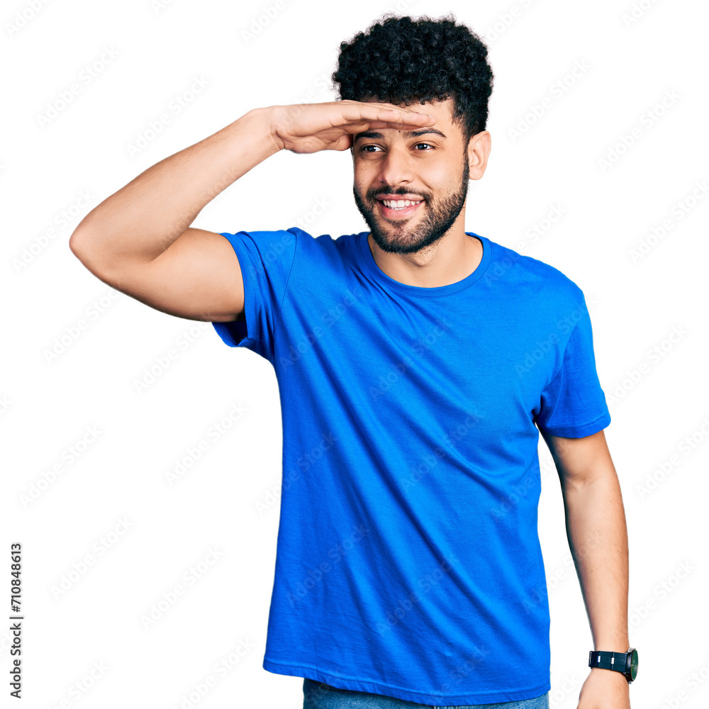 Young arab man with beard wearing casual blue t shirt very happy and smiling looking far away with hand over head. searching concept. Young arab man with beard wearing casual blue t shirt very happy and smiling looking far away with hand over head. searching concept.