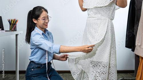 Asian woman fashion designer sewing and trying new clothes of dress on model while working