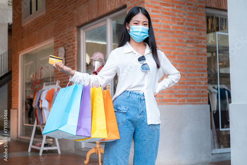 Asian woman shopaholic wearing face mask with many colorful shopping bags and holding credit card