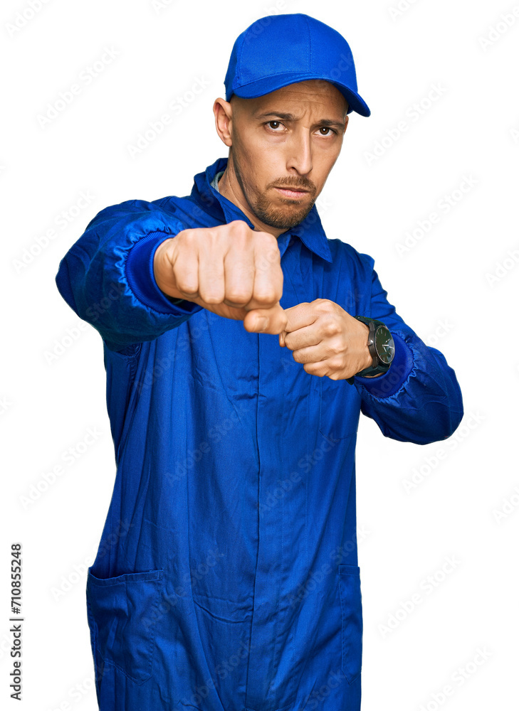 Bald man with beard wearing builder jumpsuit uniform punching fist to fight, aggressive and angry attack, threat and violence