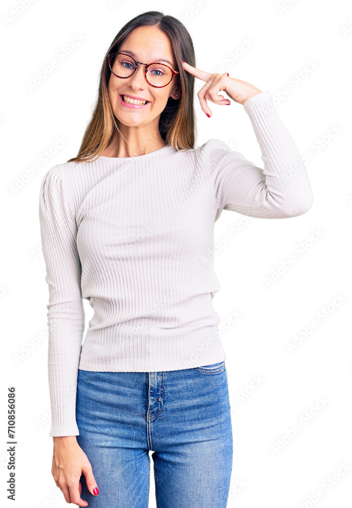 Beautiful brunette young woman wearing casual white sweater and glasses smiling pointing to head with one finger, great idea or thought, good memory Beautiful brunette young woman wearing casual white sweater and glasses smiling pointing to head with one finger, great idea or thought, good memory