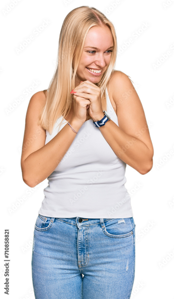 Young blonde girl wearing casual style with sleeveless shirt laughing nervous and excited with hands on chin looking to the side Young blonde girl wearing casual style with sleeveless shirt laughing nervous and excited with hands on chin looking to the side