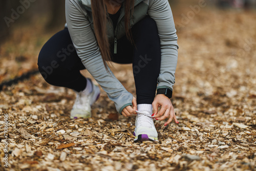 Woman Tying Her Shoelaces on a Leaf-Covered Path in Autumn