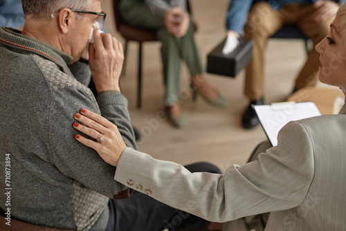 Close up of caring female therapist comforting senior man in group therapy session and putting hand on shoulder