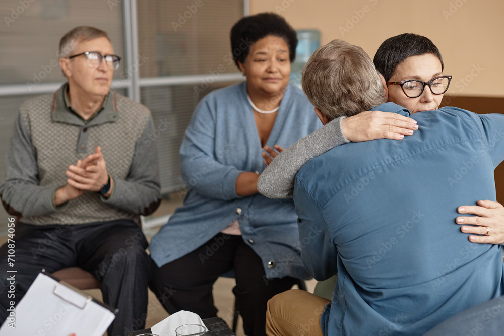 Back view of two senior people embracing in group therapy session supporting each other with mental health struggles, copy space