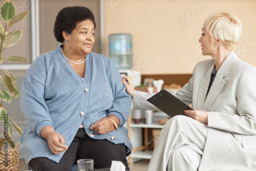 Portrait of distressed Black senior woman talking to caring female psychologist in therapy session
