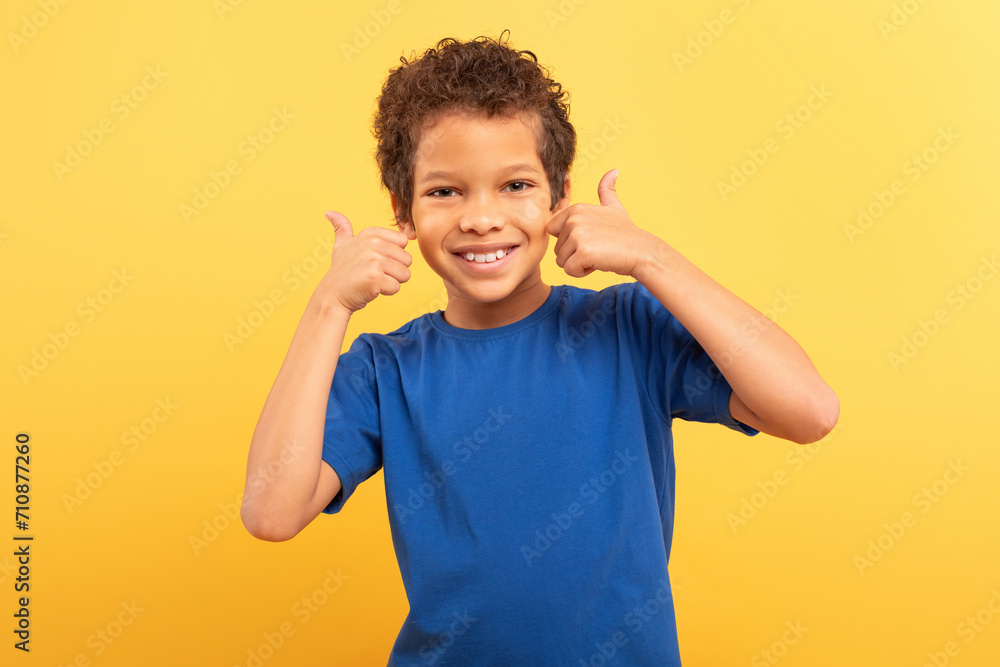 Boy with thumbs up near face, smiling on yellow background Boy with thumbs up near face, smiling on yellow background