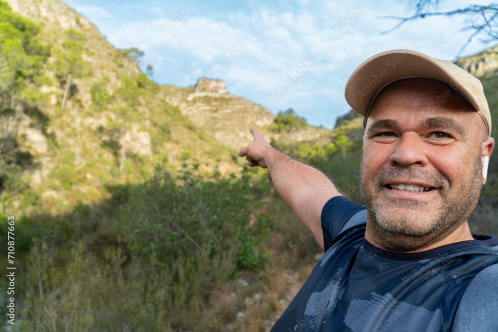 Naklejka premium Hiker man takes a photo selfie in the mountain, pointing the landscape.