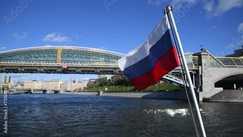 Russian national flag swaying on flagpole of sailing tourboat in a sunny autumn day in Moscow, Russia. Bridge standing on Moskva river in the background. Soft focus. Real time handheld video.