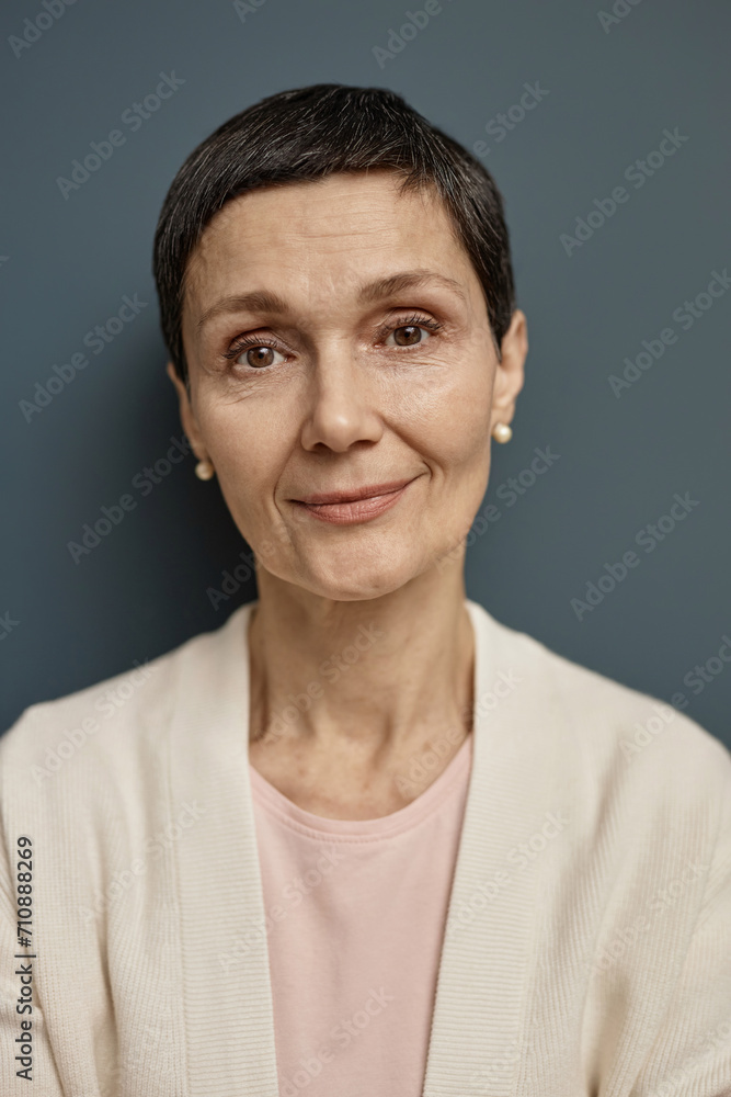 Fototapeta premium Vertical closeup portrait of mature woman looking at camera against grey background with smile