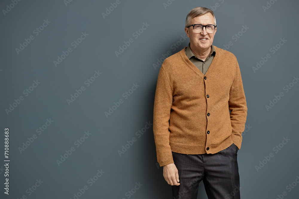 Obraz premium Front view portrait of mature man wearing glasses and looking at camera standing against grey background, copy space