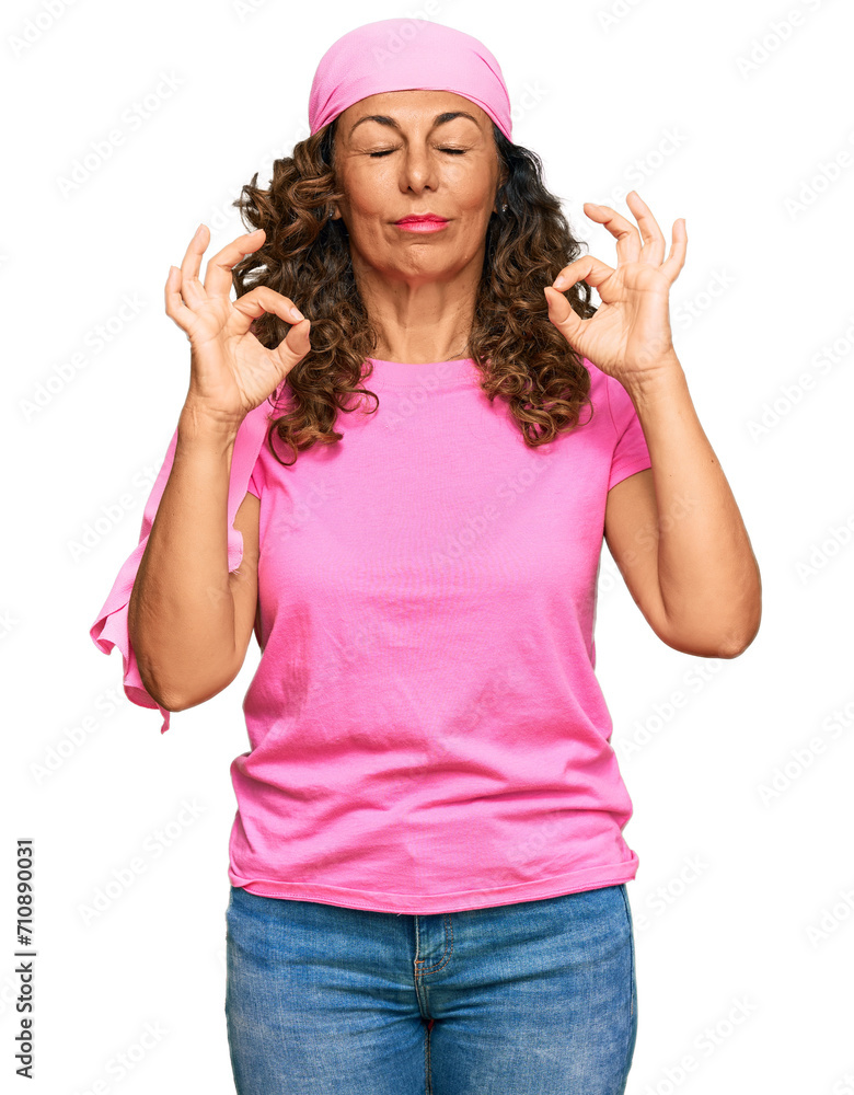 Middle age hispanic woman wearing breast cancer support pink scarf relax and smiling with eyes closed doing meditation gesture with fingers. yoga concept. Middle age hispanic woman wearing breast cancer support pink scarf relax and smiling with eyes closed doing meditation gesture with fingers. yoga concept.