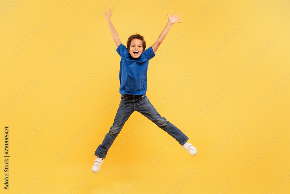 Ecstatic boy jumping high with arms up on yellow background Ecstatic boy jumping high with arms up on yellow background