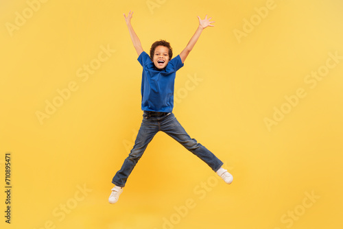 Ecstatic boy jumping high with arms up on yellow background