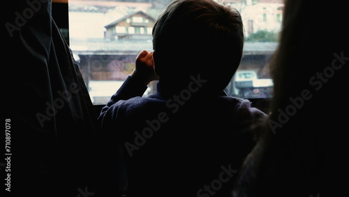 Back of pensive child observing view from train stopped at platform station. Kid traveling and daydreaming, lost in thought