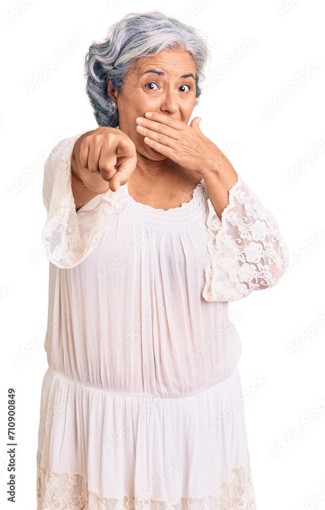 Senior woman with gray hair wearing bohemian style laughing at you, pointing finger to the camera with hand over mouth, shame expression