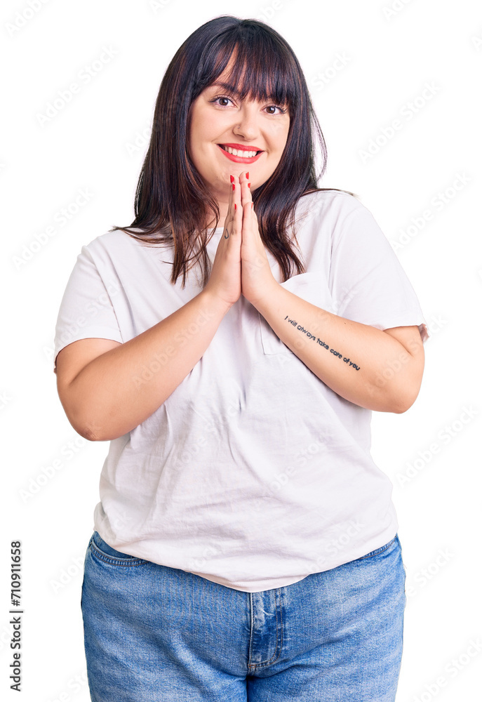 Young plus size woman wearing casual clothes praying with hands together asking for forgiveness smiling confident. Young plus size woman wearing casual clothes praying with hands together asking for forgiveness smiling confident.