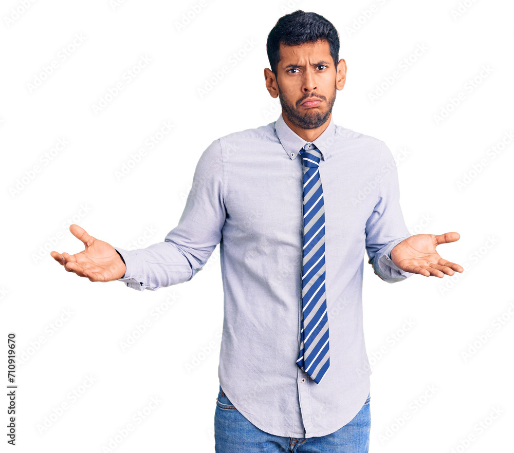 Young latin man wearing business clothes clueless and confused expression with arms and hands raised. doubt concept. Young latin man wearing business clothes clueless and confused expression with arms and hands raised. doubt concept.