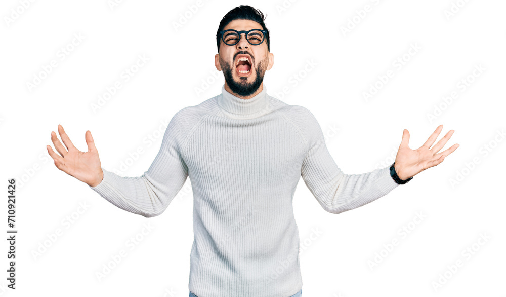 Fototapeta premium Young arab man with beard wearing elegant turtleneck sweater and glasses crazy and mad shouting and yelling with aggressive expression and arms raised. frustration concept.