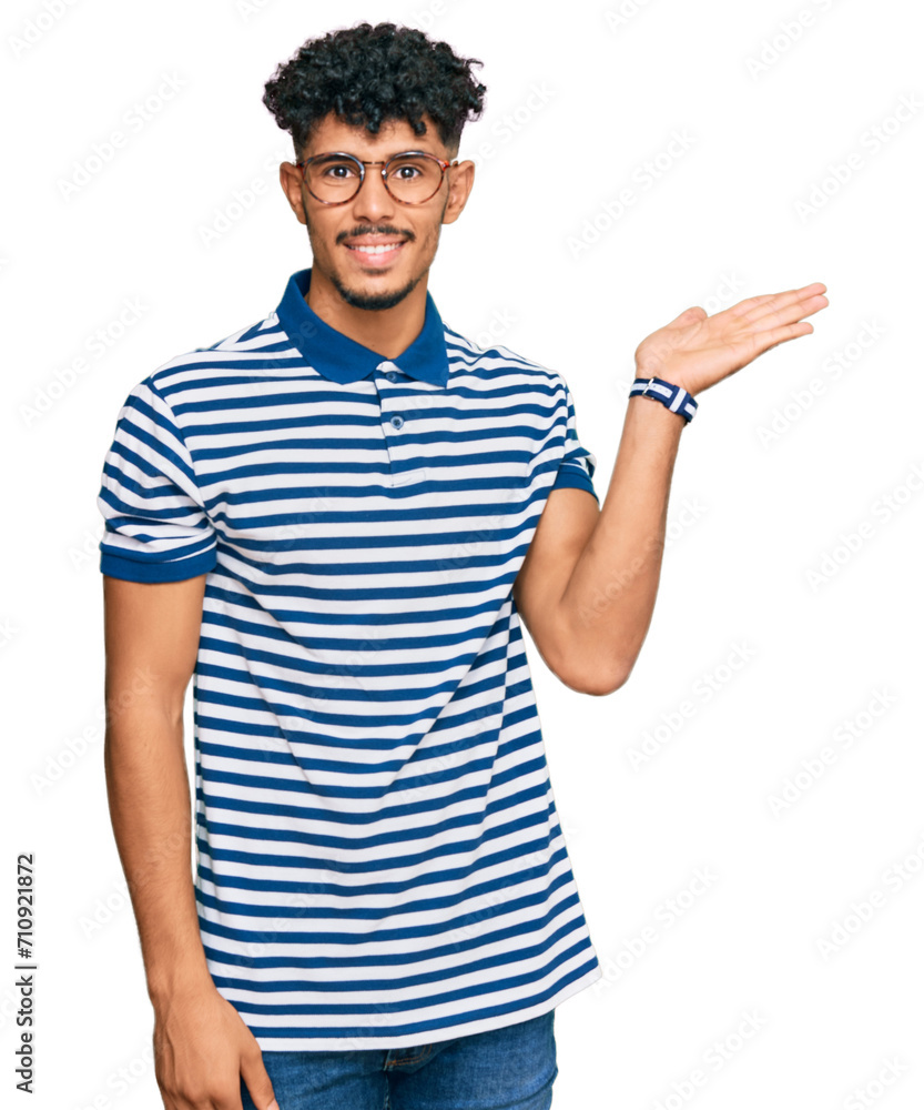 Young arab man wearing casual clothes and glasses smiling cheerful presenting and pointing with palm of hand looking at the camera. Young arab man wearing casual clothes and glasses smiling cheerful presenting and pointing with palm of hand looking at the camera.