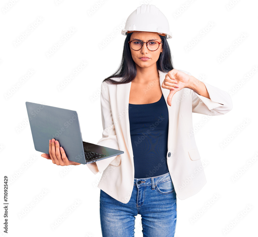 Young beautiful latin girl wearing architect hardhat holding laptop with angry face, negative sign showing dislike with thumbs down, rejection concept Young beautiful latin girl wearing architect hardhat holding laptop with angry face, negative sign showing dislike with thumbs down, rejection concept