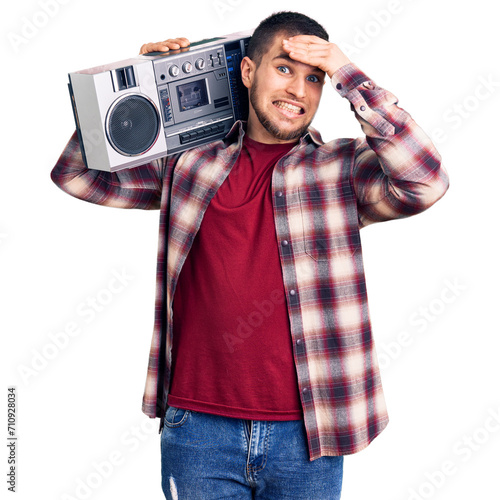 Young handsome man listening to music holding boombox stressed and frustrated with hand on head, surprised and angry face