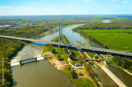 Massive pylon bridge spanning Oder river flowing by Wroclaw. Redzinski Bridge and lush greenery around city of Poland on sunny day aerial view photo