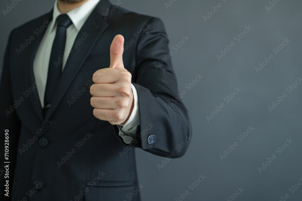 Business professional giving a thumbs-up, dressed in a dark suit against a grey backdrop Business professional giving a thumbs-up, dressed in a dark suit against a grey backdrop