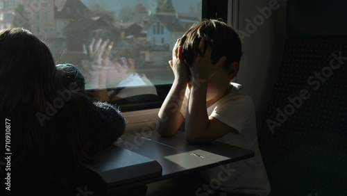 Tired Litle boy rubbing eyes and face while on a moving train hiding from sun rays. Passenger Child waking up from nap while traveling photo