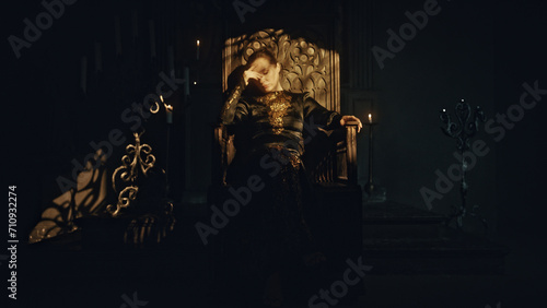 Foto A young woman in a black long dress sits in a wooden carved throne in a dark Got