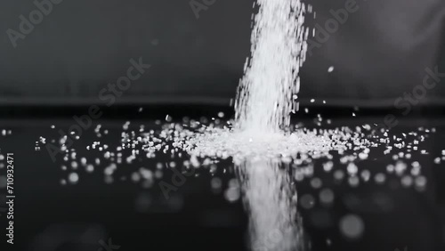 White sugar is poured onto a black glass surface. Sweet drug concept, pile of sweet particles. Close-up, slow motion photo