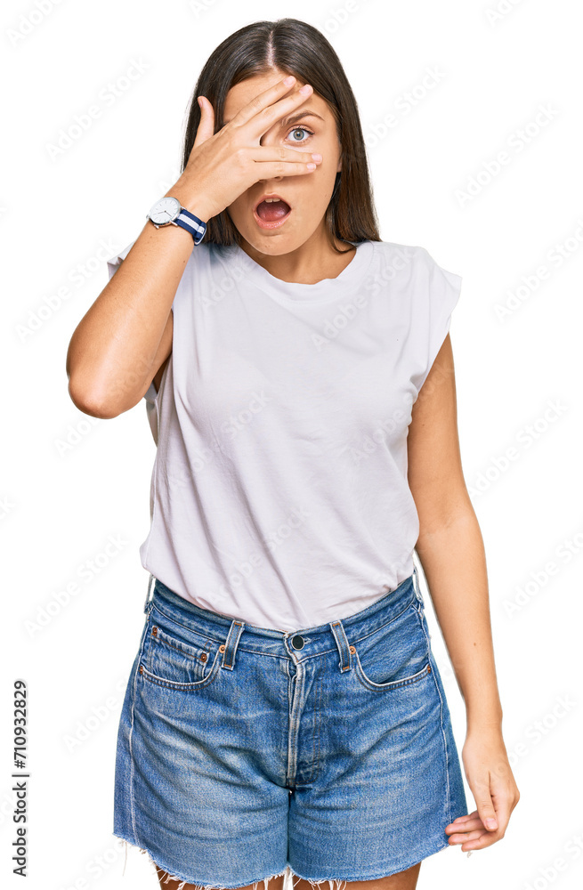 Young caucasian woman wearing casual white tshirt peeking in shock covering face and eyes with hand, looking through fingers with embarrassed expression. Young caucasian woman wearing casual white tshirt peeking in shock covering face and eyes with hand, looking through fingers with embarrassed expression.