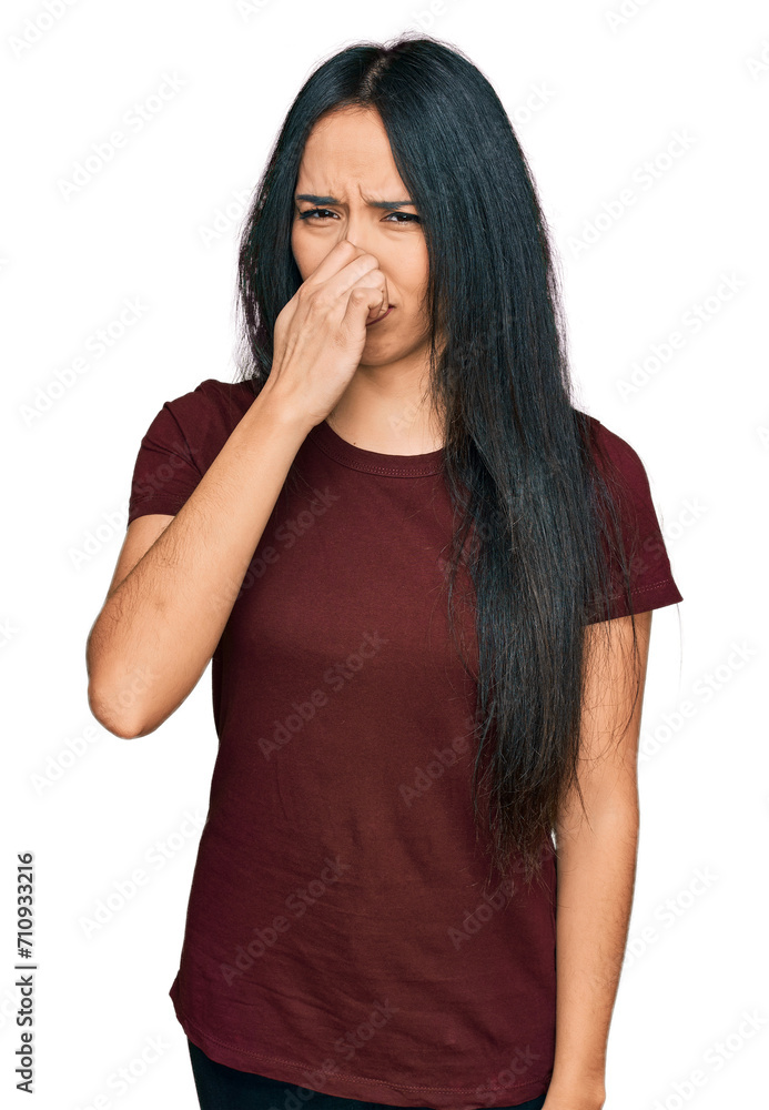 Young hispanic girl wearing casual t shirt smelling something stinky and disgusting, intolerable smell, holding breath with fingers on nose. bad smell Young hispanic girl wearing casual t shirt smelling something stinky and disgusting, intolerable smell, holding breath with fingers on nose. bad smell
