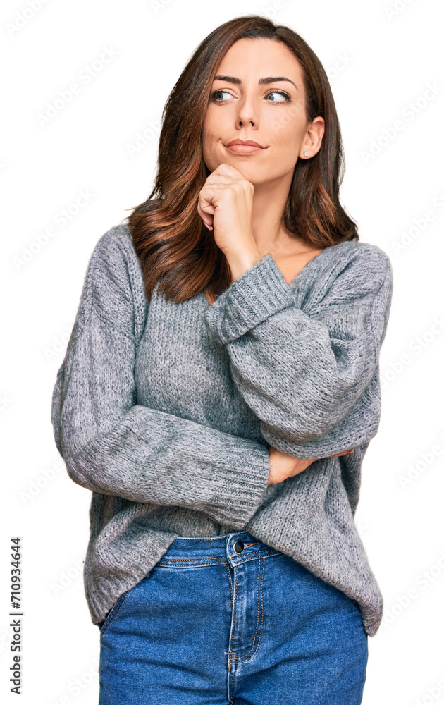 Young brunette woman wearing casual winter sweater serious face thinking about question with hand on chin, thoughtful about confusing idea Young brunette woman wearing casual winter sweater serious face thinking about question with hand on chin, thoughtful about confusing idea