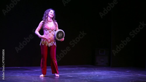 Young curly-haired woman in eastern suit finishes dance on stage. photo