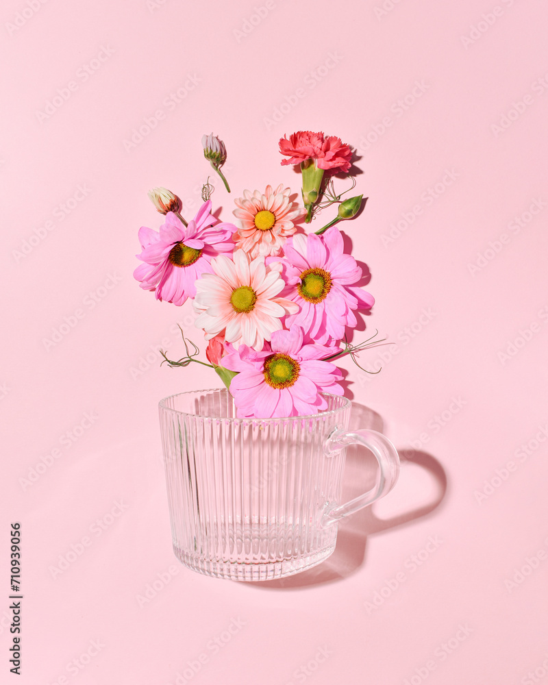 Floral composition with spring garden flowers and glass cup for tea on a candy pink background.