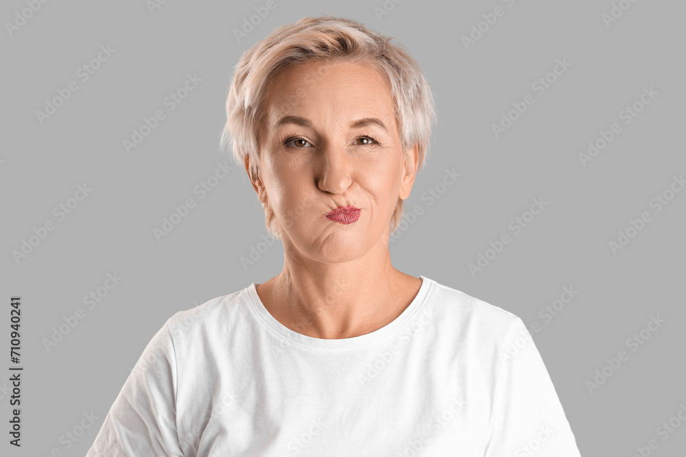 Mature woman doing face building exercise on light background, closeup Mature woman doing face building exercise on light background, closeup
